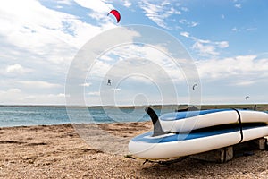 Close-up SUP board and kite equipment on sand beach shore watersport spot on bright sunny day against sea ocean coast