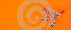Close up of supermarket grocery push cart for shopping. Shopping trolley on orange background. Concept of shopping. Copy space for