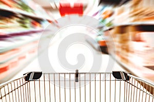 Close up of a supermarket trolley in a blurry aisle with motion blur - shopping frenzy and consumerism concept