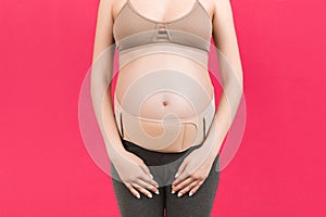 Close up of supporting orthopedic bandage against backache on pregnant woman at pink background with copy space. Orthopedic