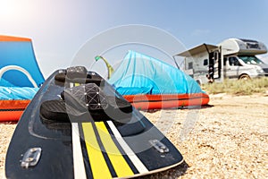 Close-up surf board and kite equipment on sand beach shore watersport spot on bright sunny day against rv camper van