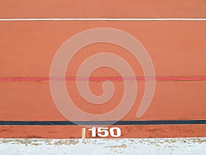 Close-up surface of orange velodrome race track with dividing lines and distance number 150 meter with copy space