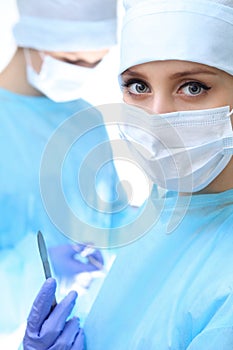 Close up of surgeon woman looking at camera while colleagues performing in background in operation room,