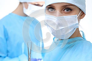 Close up of surgeon woman looking at camera while colleagues performing in background in operation room, isolated