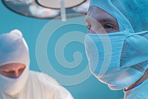 Close-up of surgeons in a sterile mask, against the background of an operating lamp, with raised hands, the surgeon`s assistant
