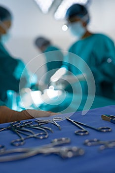 Close up of surgical instruments over diverse surgeons operating on patient in operating theatre