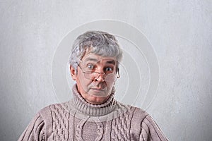 A close-up of surprised elderly man with gray hair and wrinkles wearing eyeglasses looking with wide open eyes into camera. Astoni