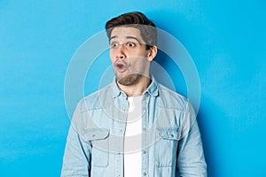 Close-up of surprised handsome man looking impressed left, open mouth fascinated, wearing casual outfit, standing over