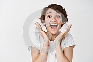 Close-up of surprised and happy woman gasping amazed, saying wow astounded, look fascinated at camera, white background