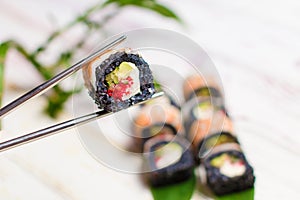 Close up of Sushi Roll piece with black rice and shrimp on top in metal chopsticks with blurred background.