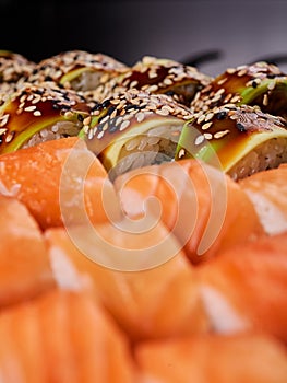 Close up of sushi rolls with avocado slices and California rolls sauce in a blurred foreground.