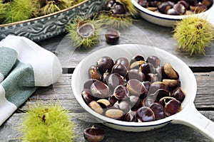 Close up of sweet chestnuts for frying in pan on wooden background