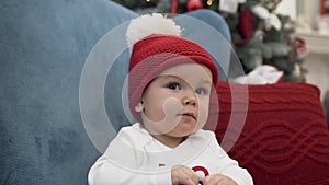 Close up of sweet toddler wearing bobble hat sitting in comfortable arm chair with pillow and playing with christmas