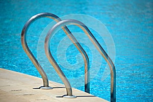 Close up of swimming pool stainless steel handrail descending into tortoise clear pool water. Accessibility of