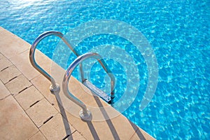 Close up of swimming pool stainless steel handrail descending into tortoise clear pool water. Accessibility of