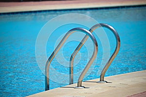 Close up of swimming pool stainless steel handrail descending into tortoise clear pool water. Accessibility of