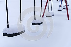 Close up of swings covered in snow at the empty playground in winter