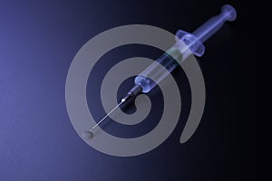Close-up of a syringe and drop in front of dark blue background