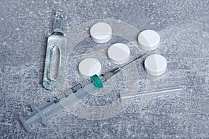 Close-up of a syringe, pills and vaccine in a capsule lie on a gray table. The concept of drugs and medication for viruses and
