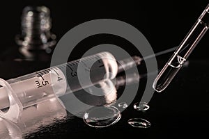 Close-up on a syringe, a pipette and few drops of fluid on dark background