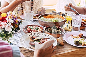 Close up of table full of fresh vegetarian vegan food with group of people eating together in friendship or parentship at home or