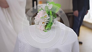 Close-up table with unrecognizable bride in wedding dress passing in slow motion leaving bridal bouquet. Blurred groom
