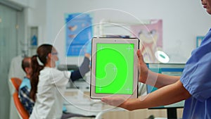 Close up of tablet with green screen display held by dental assistant