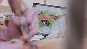 Close-up of a tablet with a picture of a ladybug on a table in a tattoo parlor.