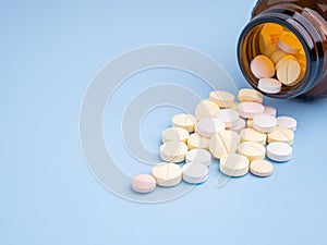 Close-up of tablets medicine spilling out of a drug bottle on a light blue background.