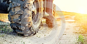 Close-up tail view of ATV quad bike on dirt country road at evening sunset time. Dirty wheel of AWD all-terrain vehicle. Travel