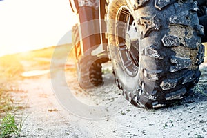 Close-up tail view of ATV quad bike on dirt country road at evening sunset time. Dirty wheel of AWD all-terrain vehicle. Travel