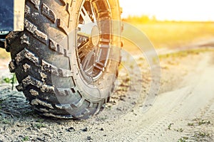 Close-up tail view of ATV quad bike on dirt country road at evening sunset time. Dirty wheel of AWD all-terrain vehicle. Travel