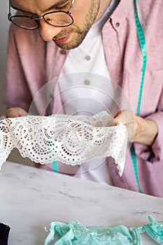 Close-up of a tailor in a pink shirt. A male designer with glasses chooses the type of lace for underwear. A self-taught seamster