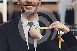 Close up. Tailor uses measuring tape to measure dimensions of customer for tailoring suit.