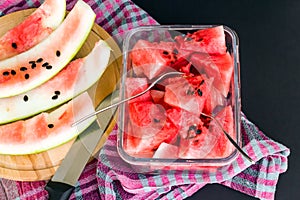 Sliced watermelon in glass container with black seeds on black background