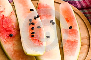 Sliced watermelon peels with black seeds on a wooden tray,