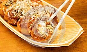 Close up of Takoyaki or octopus balls on chopsticks. Japanese food on wooden background