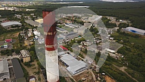 Close-up of tall, red and white chimney-stalk above the industrial zone and factory buildings surrounded by green forest
