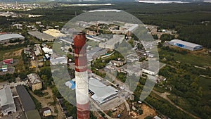 Close-up of tall, red and white chimney-stalk above the industrial zone and factory buildings surrounded by green forest