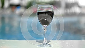 Close-up tanned female hand putting glass bocal red wine at swimming pool background slowmo