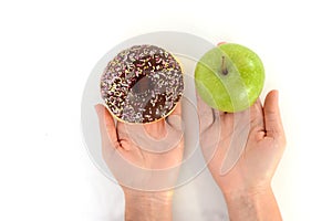 Close-up of tasty chocolate donut and fresh green apple on white background suggesting healthy eating concept