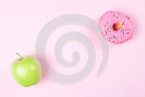 Close-up of tasty donuts and fresh green apple on pink background suggesting healthy food concept