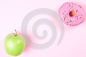 Close-up of tasty donuts and fresh green apple on pink background suggesting healthy food concept