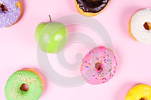 Close-up of tasty donuts and fresh green apple on pink background suggesting healthy food concept