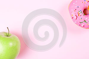 Close-up of tasty donuts and fresh green apple on pink background suggesting healthy food concept