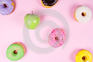 Close-up of tasty donuts and fresh green apple on pink background suggesting healthy food concept