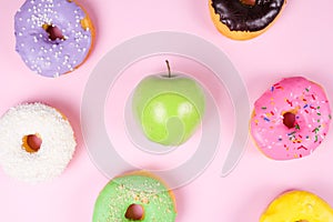 Close-up of tasty donuts and fresh green apple on pink background suggesting healthy food concept