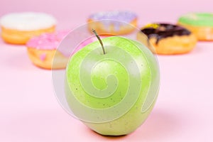 Close-up of tasty donuts and fresh green apple on pink background suggesting healthy food concept