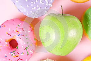 Close-up of tasty donuts and fresh green apple on pink background suggesting healthy food concept