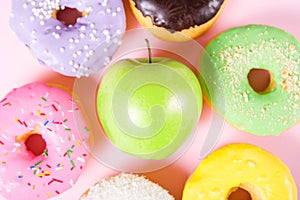 Close-up of tasty donuts and fresh green apple on pink background suggesting healthy food concept